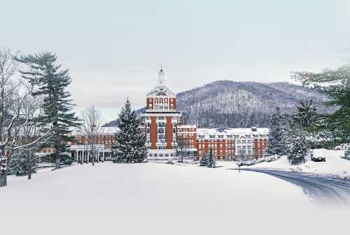 A large brick building surrounded by snow-covered trees and mountains, creating a serene winter landscape.