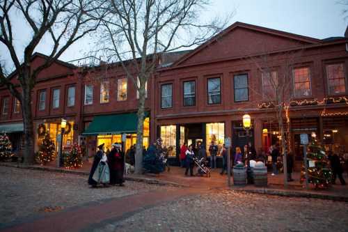 A festive street scene with decorated shops, holiday lights, and people enjoying the evening atmosphere.