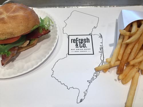 A sandwich with lettuce and tomato next to a serving of fries on a paper featuring a New Jersey outline and logo.