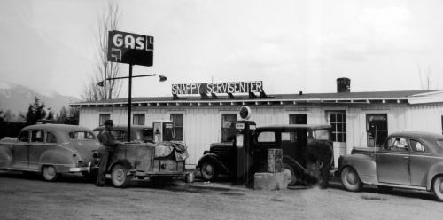 A vintage gas station with classic cars parked outside, featuring a sign that reads "Snappy Servicenter."
