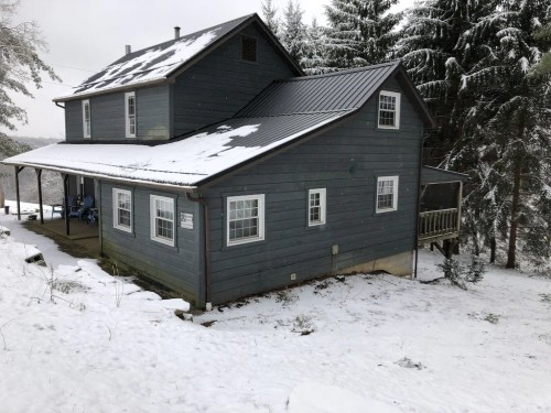 A two-story blue house surrounded by snow-covered trees and a snowy ground.