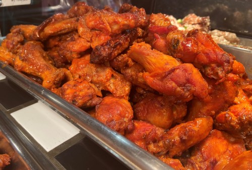 A large pile of spicy, glazed chicken wings in a metal tray, showcasing their vibrant orange color.