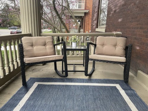 Two cushioned rocking chairs on a porch with a small table and a potted plant, surrounded by a cozy atmosphere.