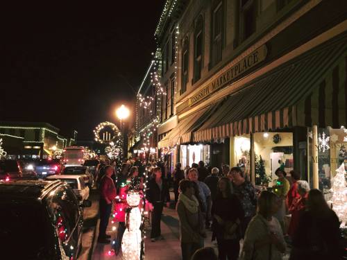 A festive street scene at night, bustling with people and adorned with holiday lights and decorations.