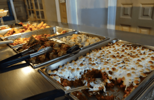 A buffet table with various dishes, including a casserole topped with marshmallows and other savory items.