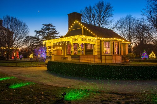 A beautifully lit house adorned with colorful holiday lights, surrounded by festive decorations and trees at dusk.