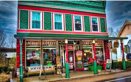 Colorful vintage storefront with signs for antiques, coffee, candy, and ice cream, set against a cloudy sky.