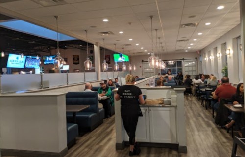A restaurant interior with booths, patrons dining, and a server in a black shirt. TVs are visible in the background.