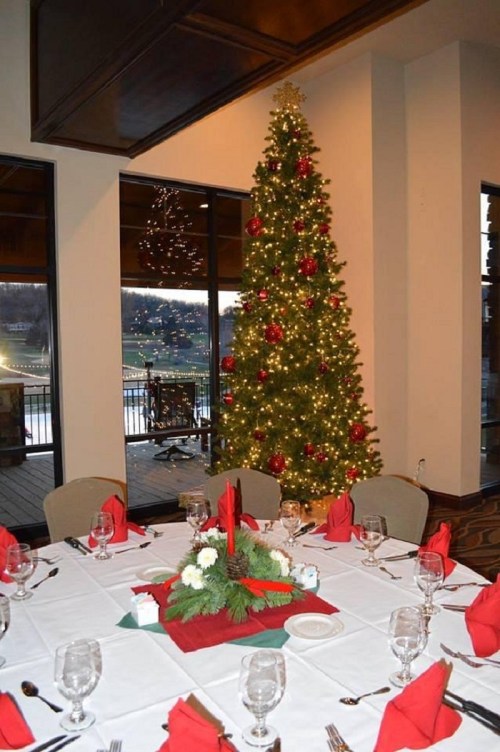 A festive dining setup with a decorated Christmas tree and a table set with red napkins and floral centerpiece.