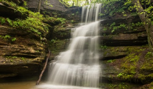 A serene waterfall cascading over rocky cliffs, surrounded by lush green foliage and trees.