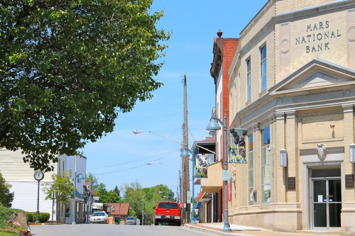 A sunny street view featuring Mars National Bank, lined with trees and small shops in a quaint town.