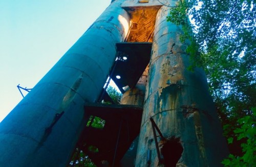 A weathered, tall structure with peeling paint, surrounded by trees, illuminated from above.
