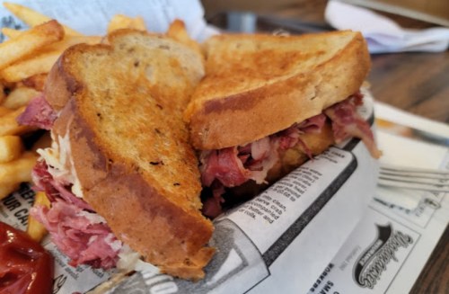 A close-up of a toasted sandwich filled with meat, served with a side of golden fries and ketchup.