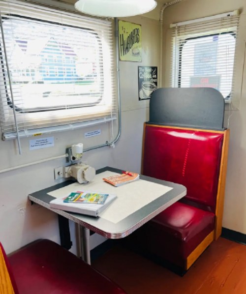 Cozy diner booth with red seats, a small table, and a sewing machine in a well-lit, vintage-style interior.