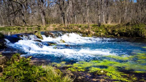 A serene river with cascading waterfalls, surrounded by trees and vibrant green vegetation.