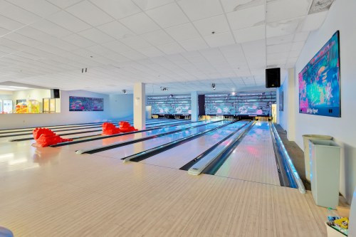 A brightly lit bowling alley with colorful lanes and two red bowling balls at the end of the lane.
