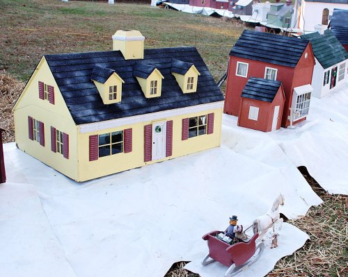 A miniature village scene featuring colorful toy houses and a horse-drawn sleigh on a white tarp.