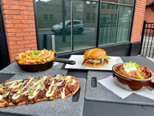 A spread of delicious food: loaded fries, a burger, a flatbread, and a bowl of chili, all on a table outside.