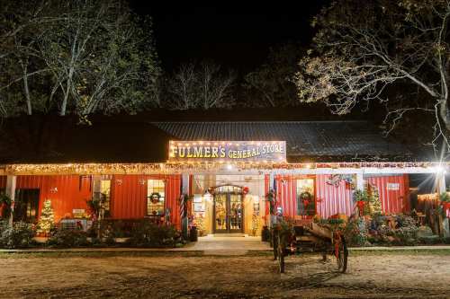 A festive general store at night, adorned with holiday lights and decorations, surrounded by trees.