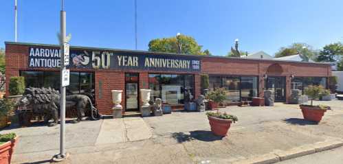 A brick building with a sign celebrating 50 years of an antique store, surrounded by potted plants and sculptures.