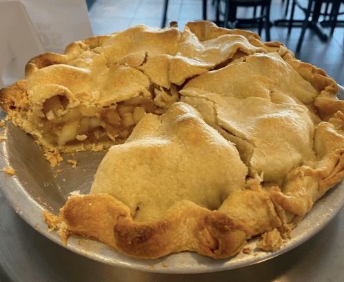 A freshly baked apple pie with a golden crust, partially sliced, revealing the apple filling inside.