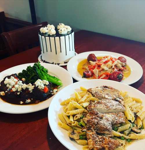 A table with a variety of dishes: pasta with chicken, stuffed peppers, meatballs, and a decorated cake.