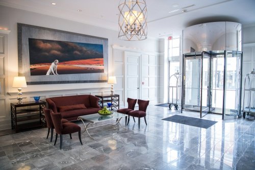 A stylish hotel lobby featuring a large painting, a sofa, two chairs, and a revolving door.