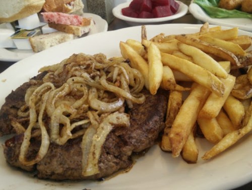 A plate featuring a juicy hamburger topped with sautéed onions, served alongside crispy French fries.