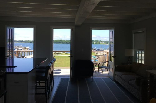A cozy interior with a view of a lake, featuring open doors, a sofa, and a kitchen bar.