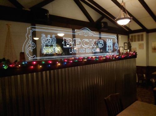 Neon sign for Beck's Land and Sea House, decorated with colorful lights in a cozy restaurant setting.