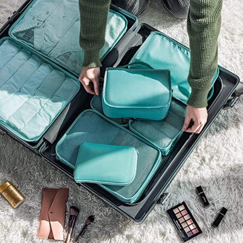 A person organizing turquoise packing cubes inside an open suitcase on a fluffy white rug.