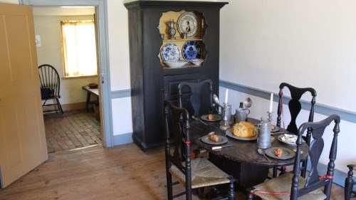 A rustic dining room with a round table set for a meal, a black cabinet, and a doorway leading to another room.