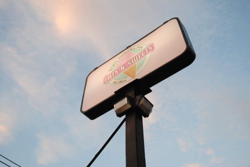 Sign for "Eats & Sweets" against a blue sky, mounted on a tall pole.