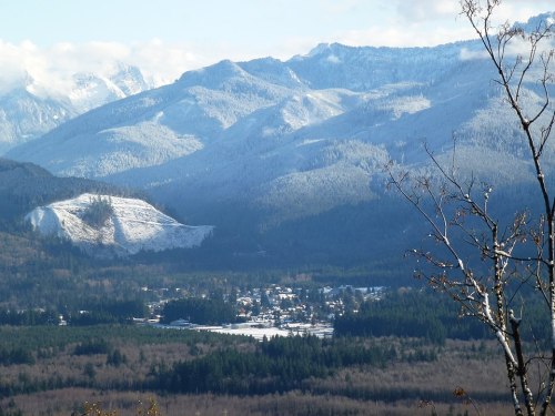 A scenic view of snow-capped mountains overlooking a small village surrounded by dense forests.