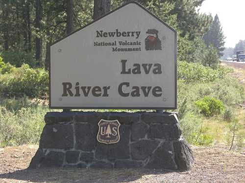 Sign for Lava River Cave at Newberry National Volcanic Monument, surrounded by trees and greenery.