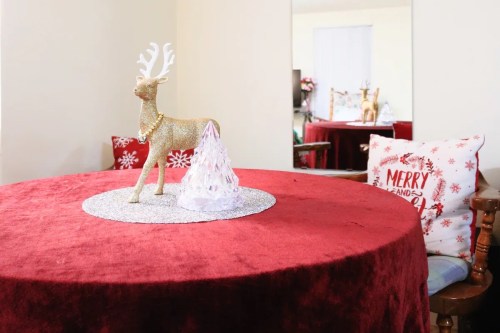 A festive table with a red tablecloth, featuring a gold reindeer and a decorative tree centerpiece.