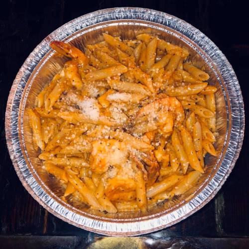A foil container filled with penne pasta topped with shrimp and grated cheese.