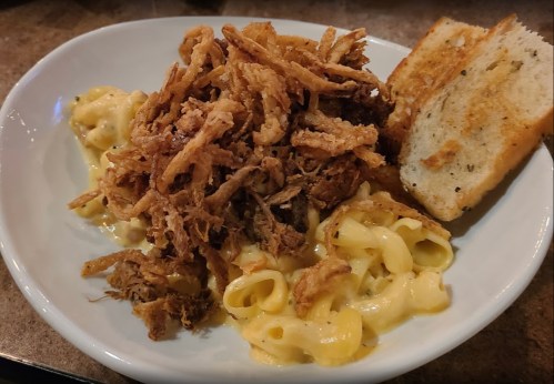A bowl of creamy macaroni and cheese topped with crispy fried onions, served with toasted garlic bread on the side.