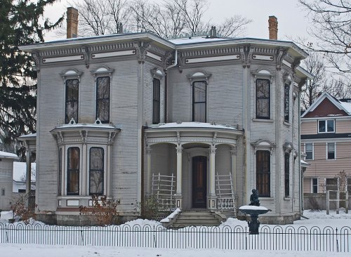 A large, historic house with ornate architecture, surrounded by snow and a decorative fence.