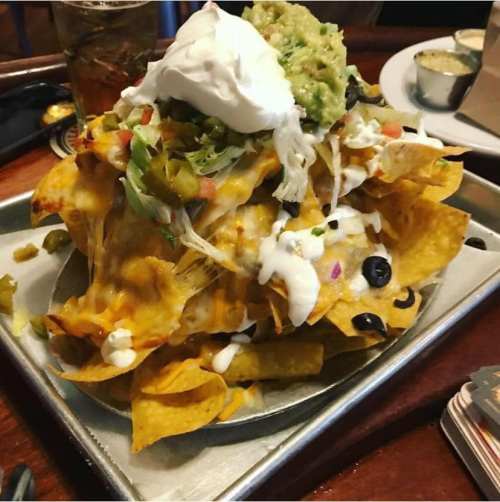 A large plate of nachos topped with cheese, guacamole, sour cream, jalapeños, and fresh vegetables.