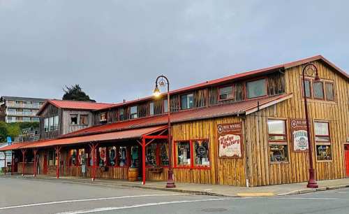 A rustic wooden building with red accents, featuring shops and a street lamp, set against a cloudy sky.