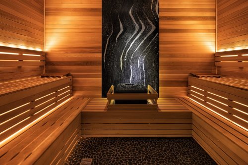 A serene sauna interior with wooden benches, soft lighting, and a striking stone wall feature.