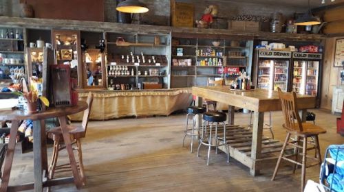 A rustic interior of a store with wooden shelves, a counter, and various products displayed.