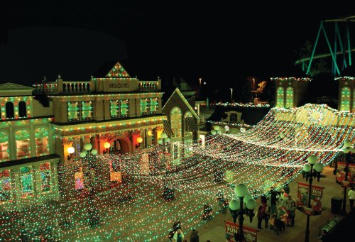 A festive night scene of a theme park adorned with colorful holiday lights and decorations.