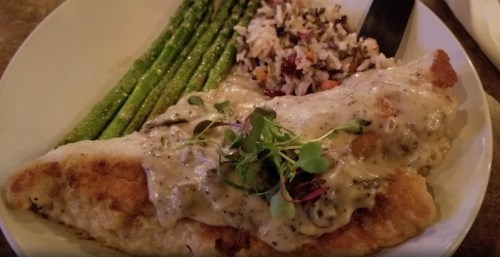 A plate featuring a fish fillet with creamy sauce, asparagus, and a side of rice with vegetables.