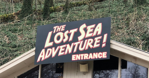 Sign for "The Lost Sea Adventure!" with "ENTRANCE" below, set against a green, wooded background.