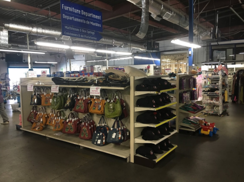 A retail store interior featuring shelves of bags and clothing, with a sign for the Furniture Department above.