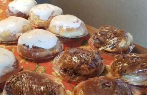 A variety of frosted pastries wrapped in plastic, arranged on a floral tablecloth.