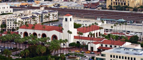 Aerial view of a building with a clock tower, surrounded by palm trees and urban architecture.