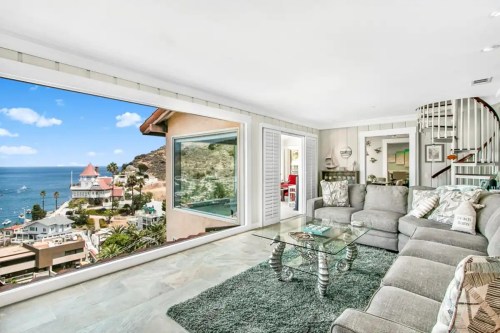 Modern living room with a large window showcasing a coastal view, featuring a gray sofa and glass coffee table.